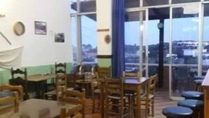 Un restaurante con mesas y sillas de madera, ventanas amplias y vistas a la ciudad.