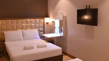 Une chambre d’hôtel avec un grand lit, un téléviseur à écran plat fixé au mur et une table de chevet avec une lampe.