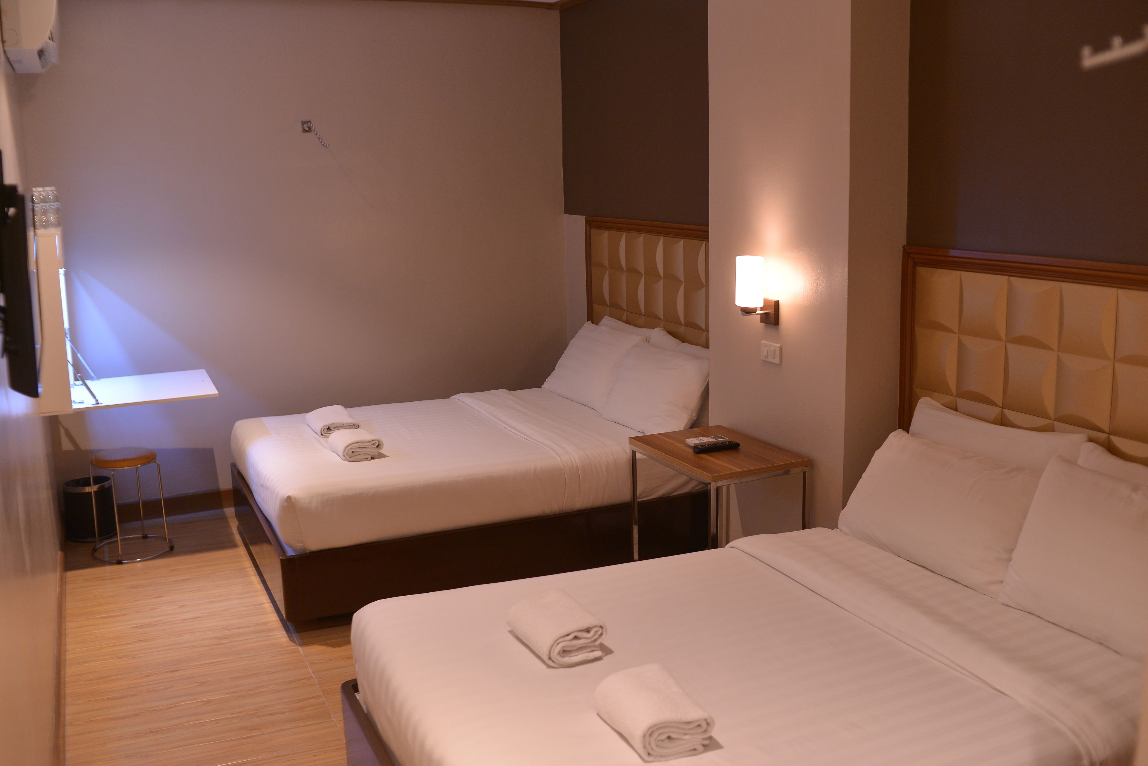 A hotel room with two beds, a small table, and a wall-mounted lamp.