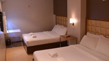 A hotel room with two beds, a small table, and a wall-mounted lamp.