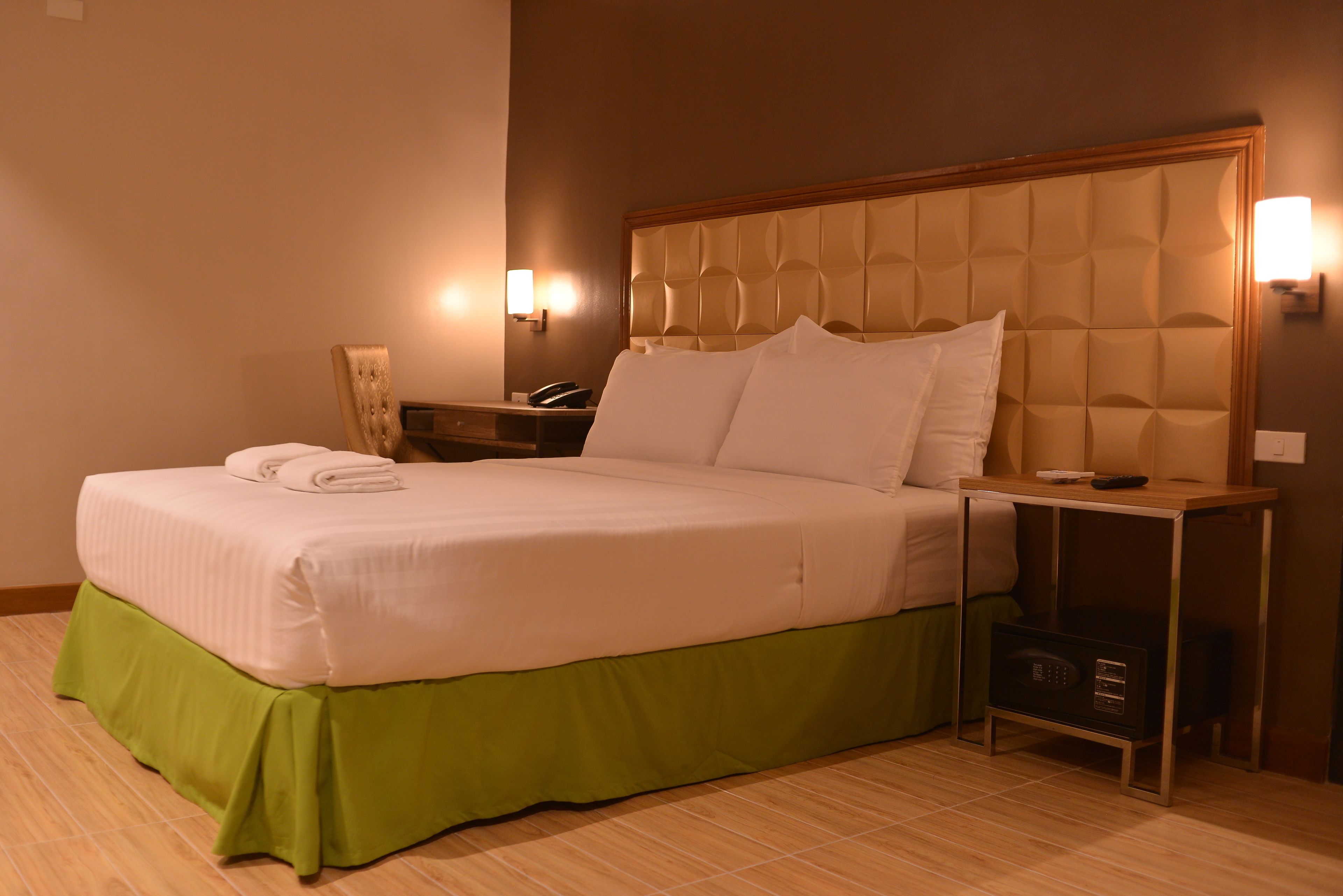 A neatly made bed with a green skirt, a bedside table with a lamp, and a wall-mounted phone.