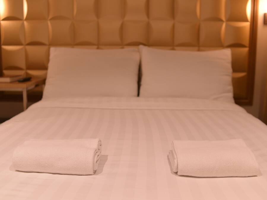 A neatly made bed with two folded towels, a headboard with a tufted design, and a bedside table with a lamp.