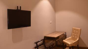 A room with a flat-screen TV mounted on the wall, a small wooden table, and a cushioned chair.