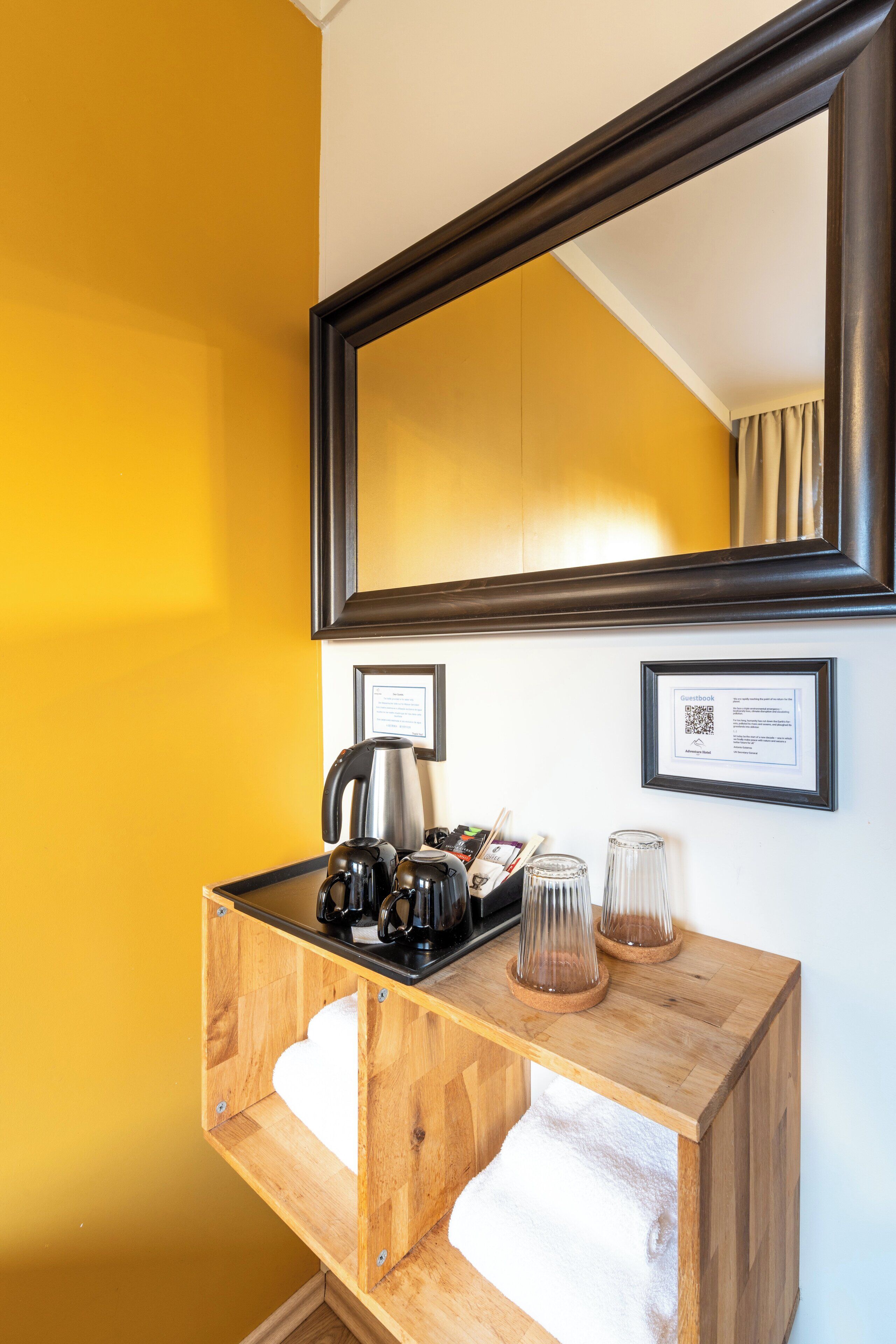 A wooden console table with a kettle, coffee maker, and glassware against a yellow wall.