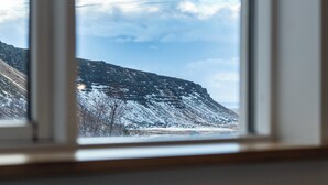 Blick durch ein Fenster auf eine verschneite Landschaft mit Bergen und blauem Himmel.