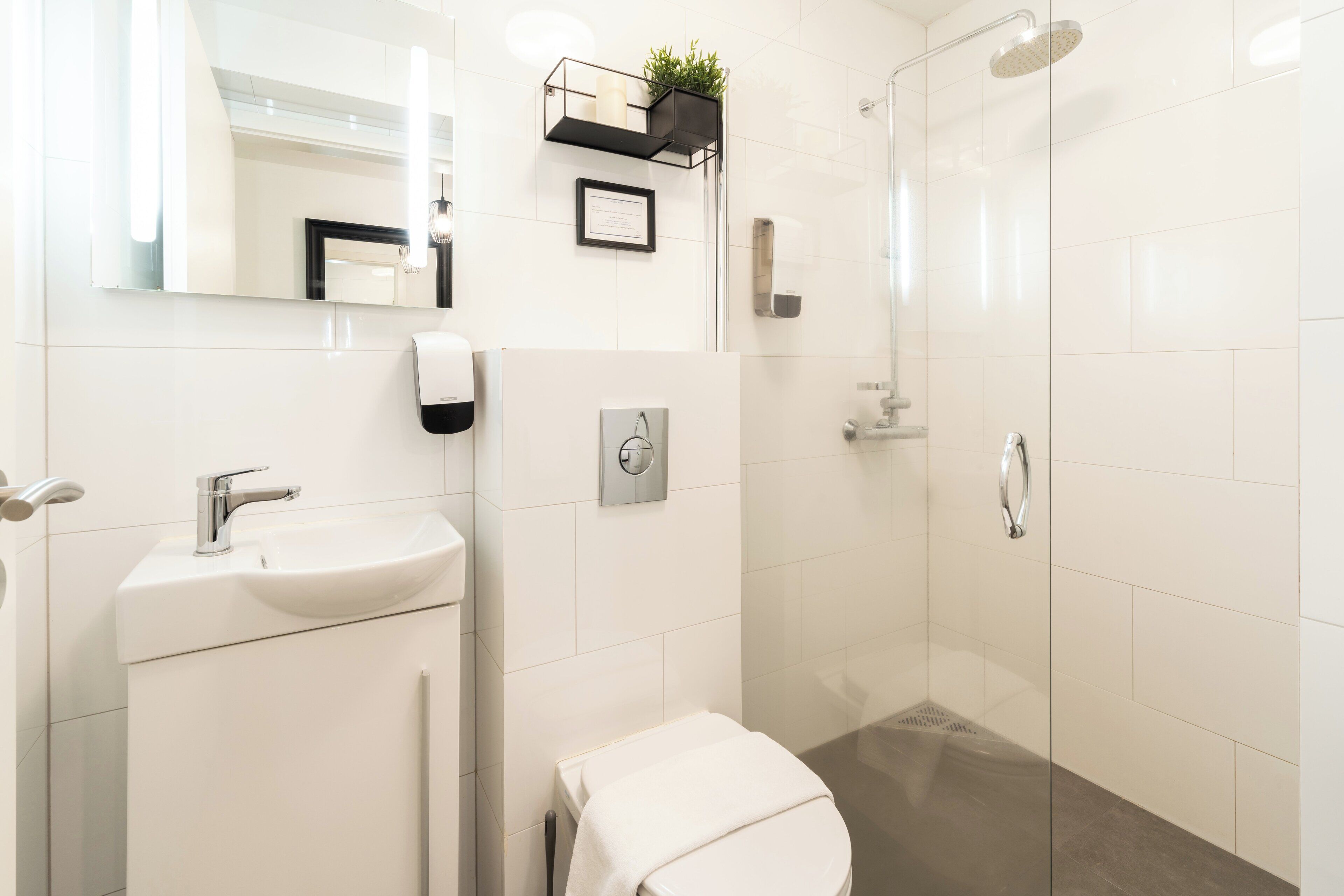 Ein modernes Badezimmer mit Waschbecken, Toilette und Dusche, alles in Weiß.