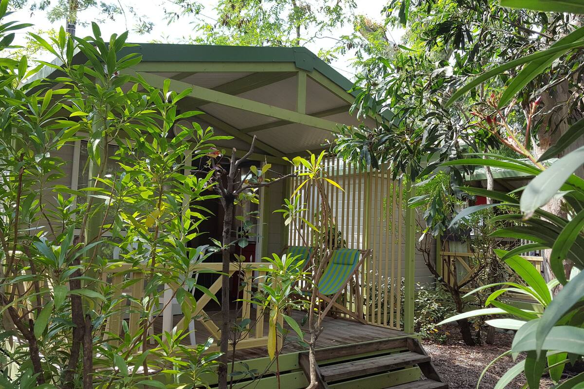A wooden gazebo with a sloped roof, surrounded by dense foliage and trees.