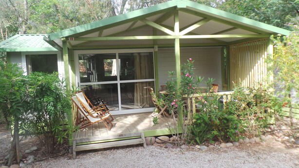 Un área de estar al aire libre con techo, con una mesa y sillas, rodeada de vegetación y un sendero de grava.