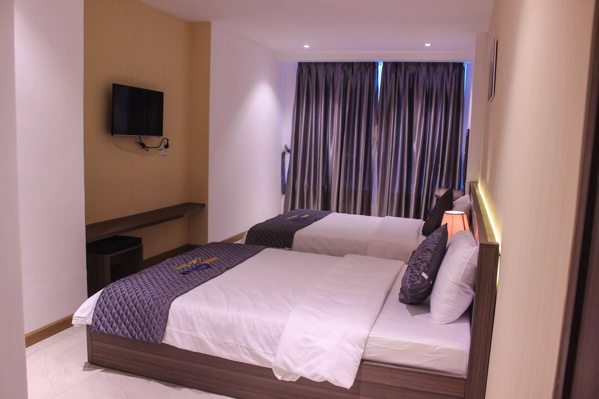 Una habitación de hotel con dos camas, un televisor montado en la pared y una cortina cubriendo la ventana.