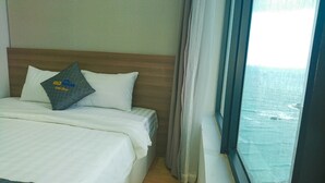 Una habitación de hotel con cama, almohada con texto, ventana con cortinas y vista al océano.