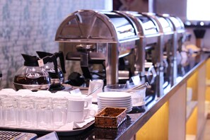 A buffet setup with multiple coffee machines, a variety of cups and plates, and a wicker basket. - Gold Oceanus Nha Trang (Bac Nha Trang)