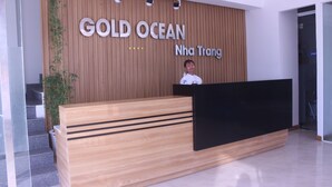 Una recepción con detalles de madera y adornos negros, un cartel que dice "GOLD OCEAN Nha Trang", y una escalera que sube a un nivel superior.