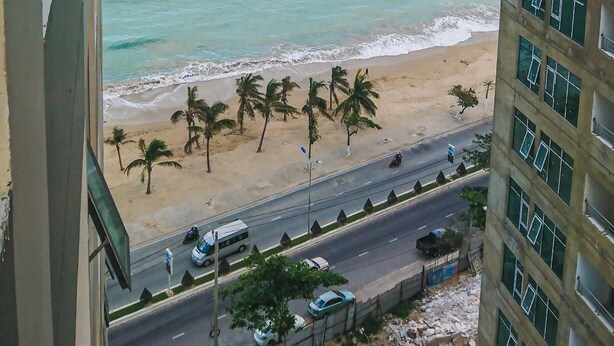 Vista costera desde un edificio alto, con una playa, palmeras y una carretera con vehículos.