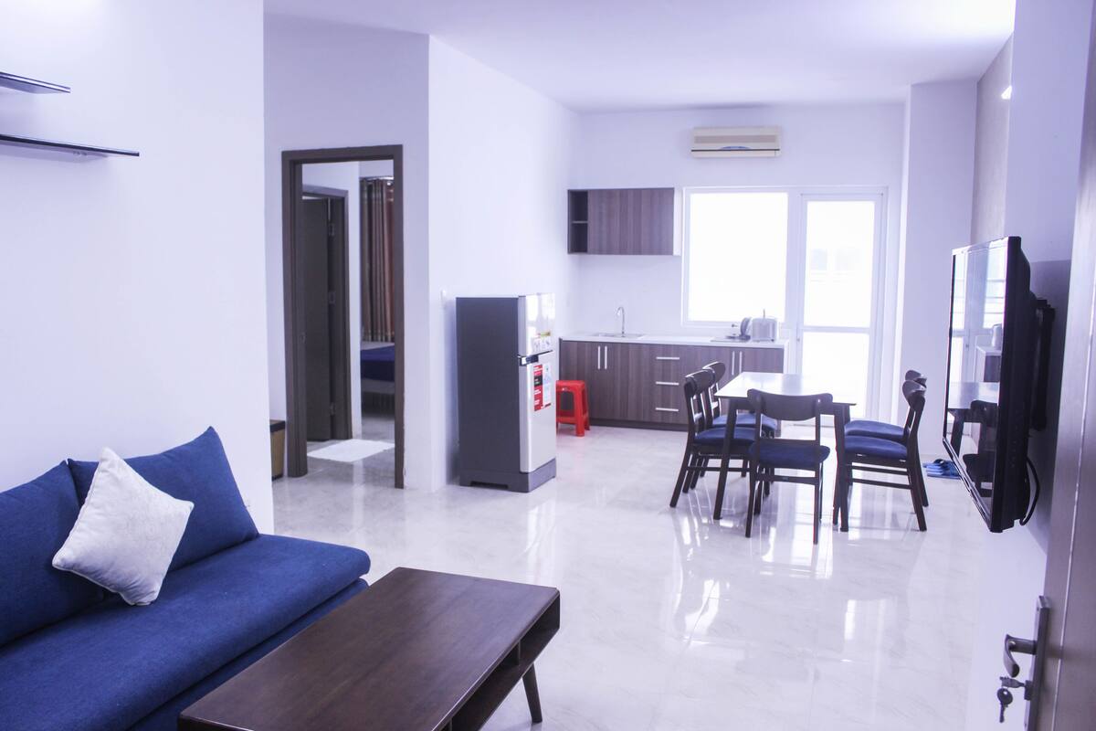 Una sala de estar moderna con un sofá azul, una mesa de centro de madera y un comedor con una mesa y sillas.