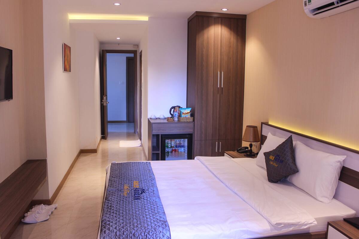 Una habitación de hotel con cama, escritorio con lámpara, armario y televisión en la pared.