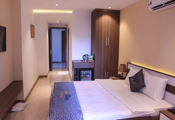 Une chambre d’hôtel avec un lit, un bureau doté d’une lampe, une armoire et un téléviseur fixé au mur.