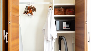 A compact room with a wooden wardrobe, a vacuum cleaner, a pet bed, and a small shelf with baskets. - The One Osaka Nipponbashi East (Osaka)