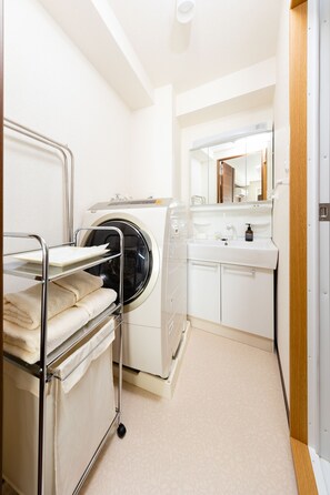 A compact laundry area with a washing machine, a drying rack, and a sink with a mirror.