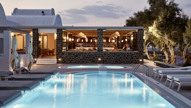 A pool area with lounge chairs, a bar, and a stone wall.