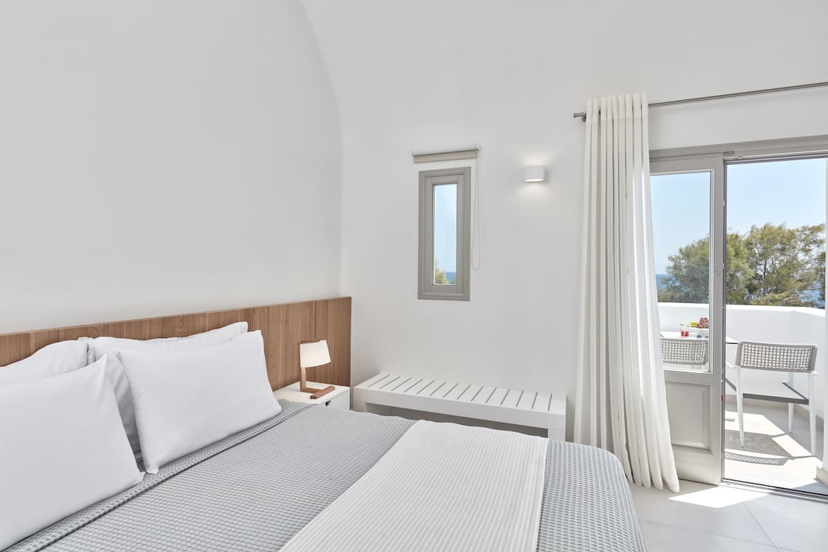 Une chambre avec un grand lit, une table de chevet, une fenêtre et une vue sur le balcon extérieur.