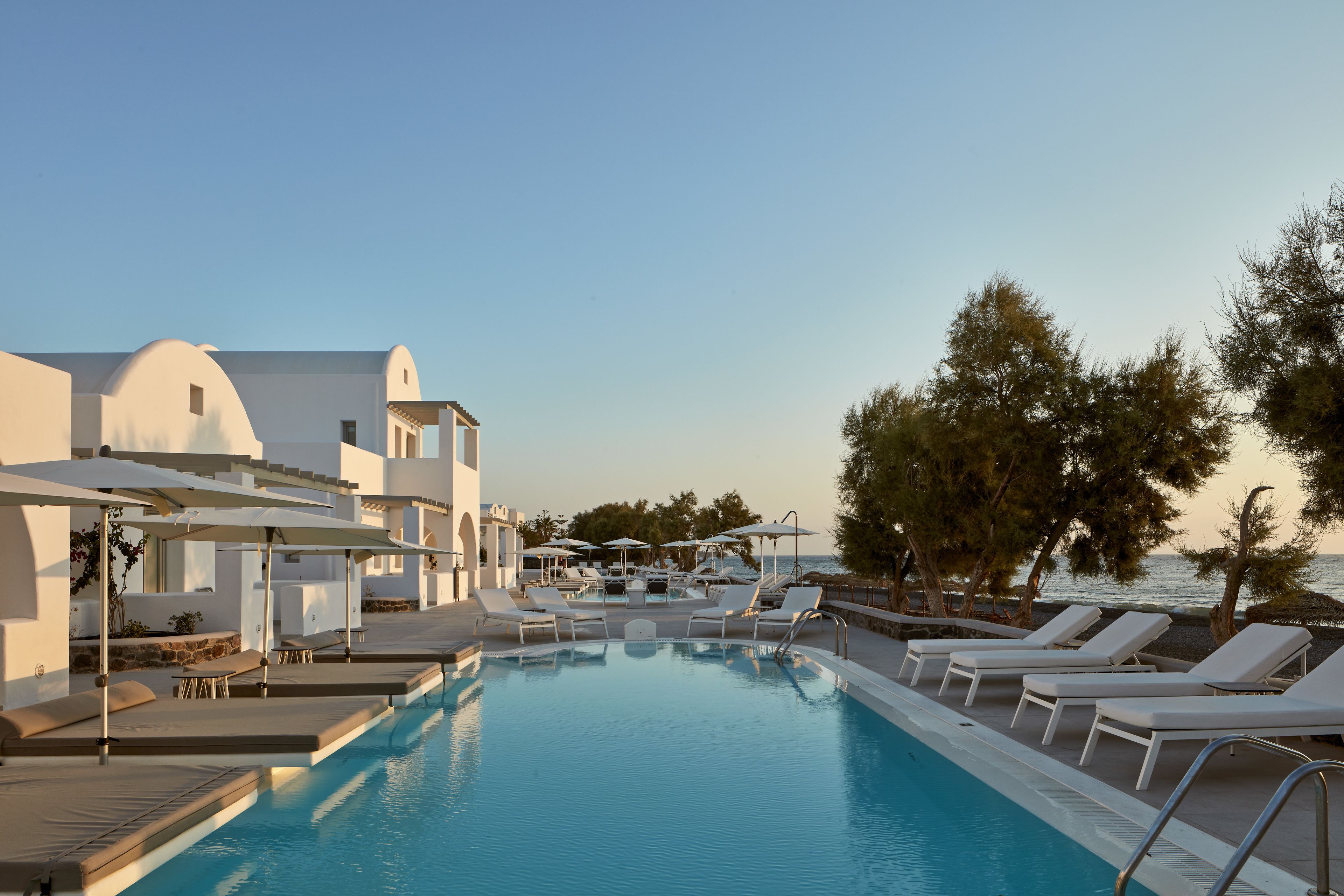 A pool area with lounge chairs and umbrellas, surrounded by white buildings and trees.