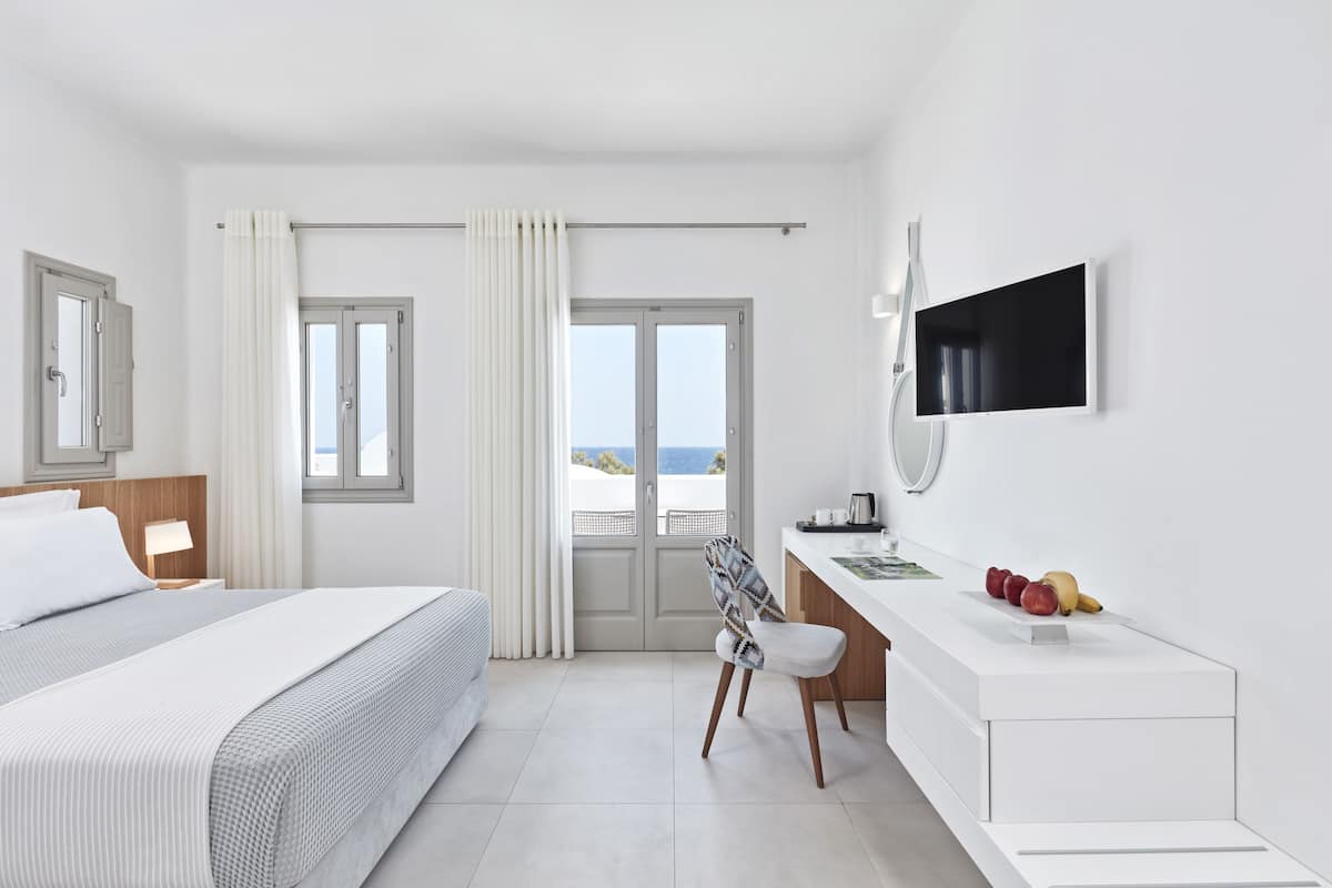 Une chambre d’hôtel moderne équipée d’un lit, d’un bureau, d’une chaise, d’une télévision et offrant une vue sur la mer.