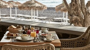 A breakfast table with various food items and drinks, overlooking a beach with umbrellas and lounge chairs.
