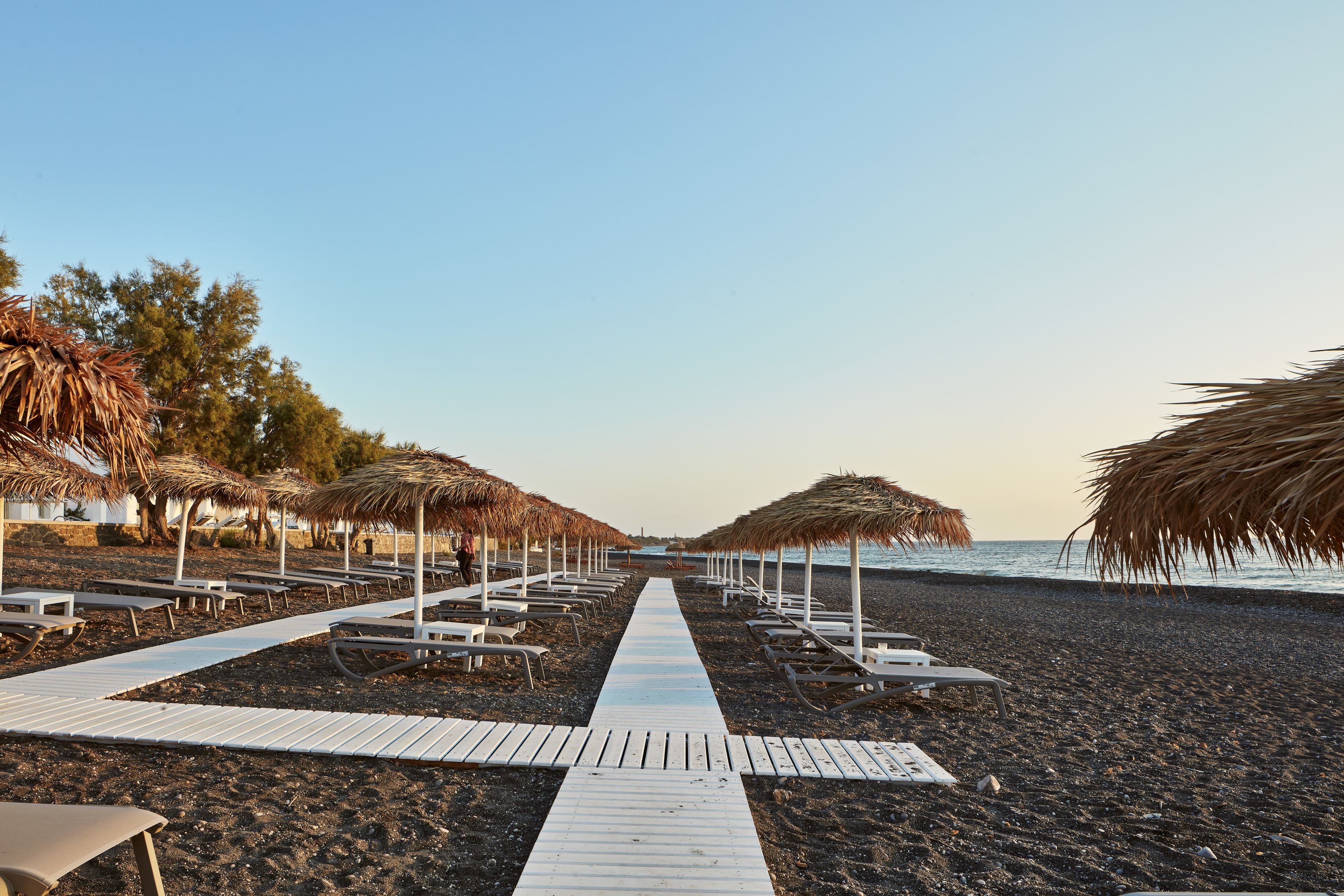 A beach walkway with thatched umbrellas and lounge chairs.