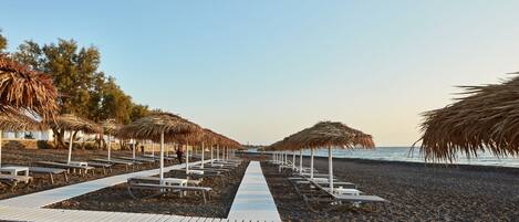 A beach walkway with thatched umbrellas and lounge chairs.