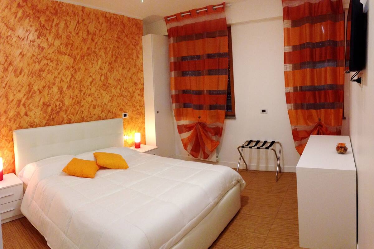 Une chambre avec un grand lit, une table de chevet avec une lampe, une petite table et une chaise.