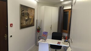 Quarto pequeno e moderno com uma escrivaninha branca, cadeira de escritório preta e um quadro grande emoldurado na parede.