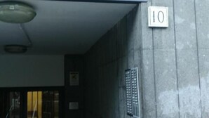 Entrada de um edifício de concreto com portão de metal, uma placa com o número 10 e corrimão de metal.
