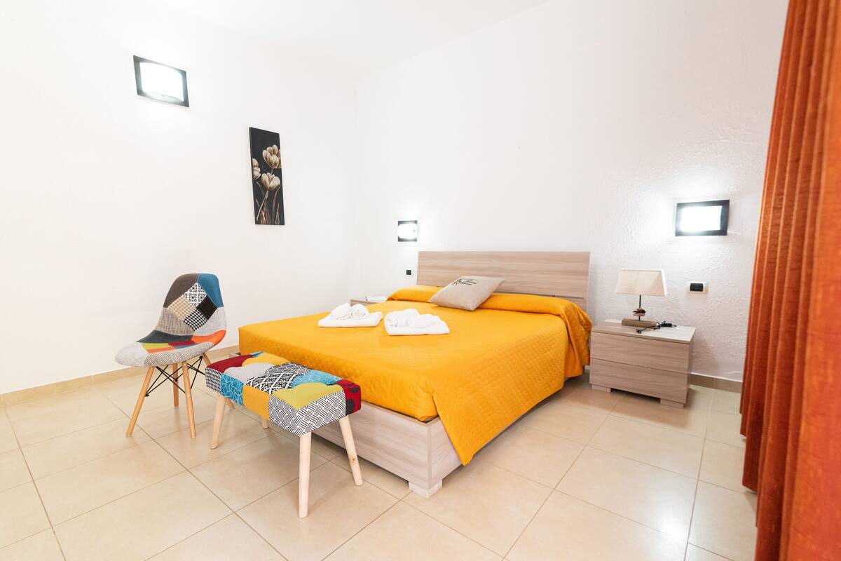 Une chambre bien rangée, avec un lit, des tables de chevet, une chaise et une petite table.