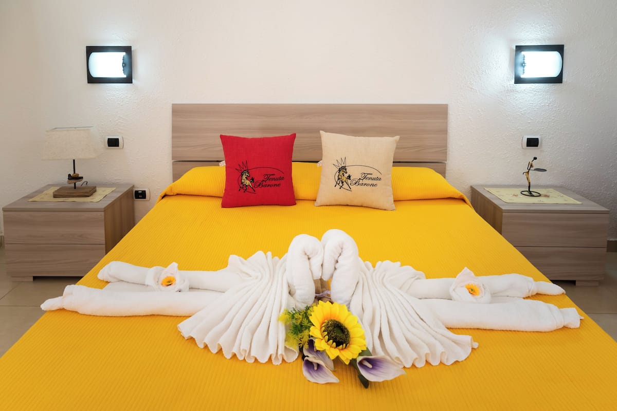Une chambre d’hôtel avec un grand lit, deux oreillers, une table de chevet avec une lampe et un luminaire fixé au mur.