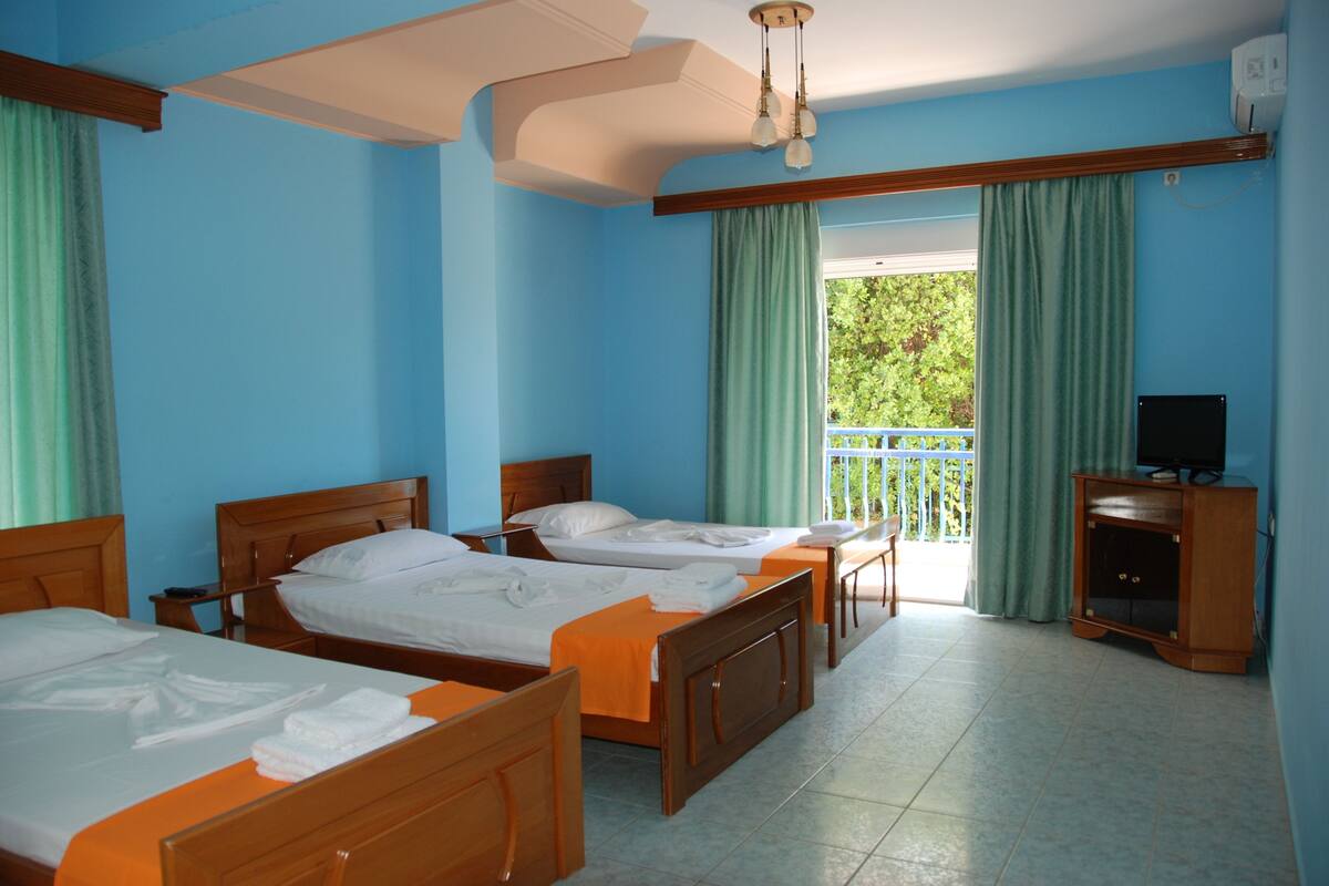 A hotel room with three wooden beds, a television, and a balcony with curtains.