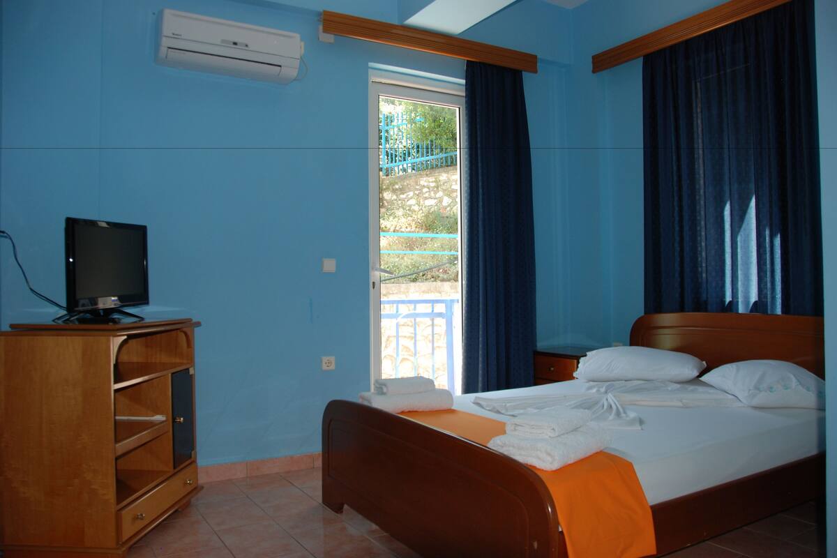 A bedroom with a bed, a television on a wooden cabinet, and a window with curtains.