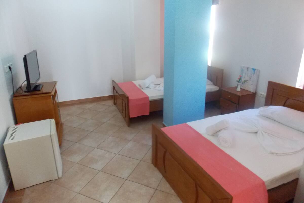 A hotel room with two beds, a TV, a desk, and a small heater.