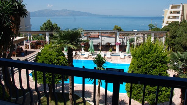 A pool area with lounge chairs and umbrellas, surrounded by greenery and overlooking a body of water.