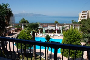 Zona de piscina con sillones de playa y sombrillas, rodeada de vegetación y con vista a un cuerpo de agua.