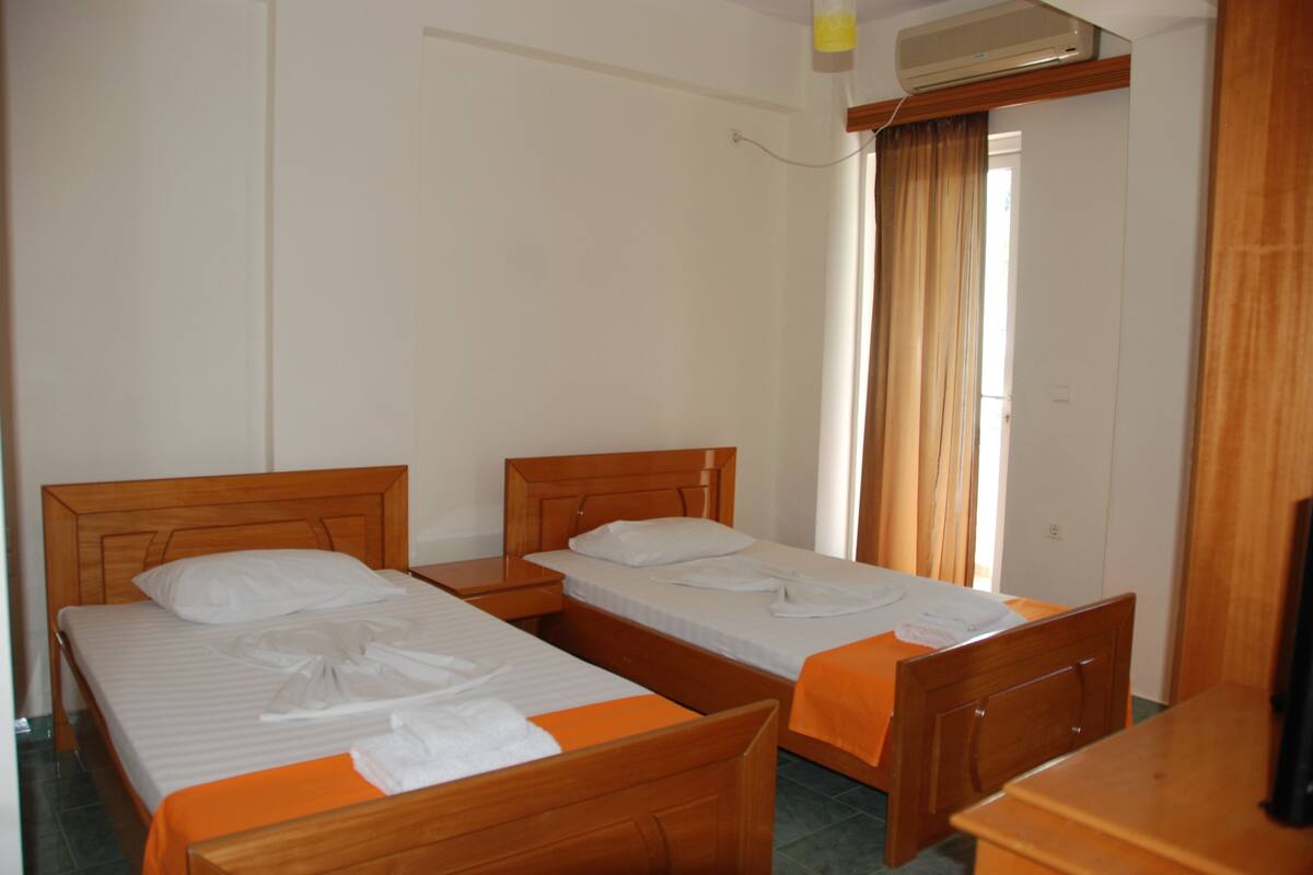 A hotel room with two wooden beds, a wooden nightstand, a wooden dresser, and a window with curtains.