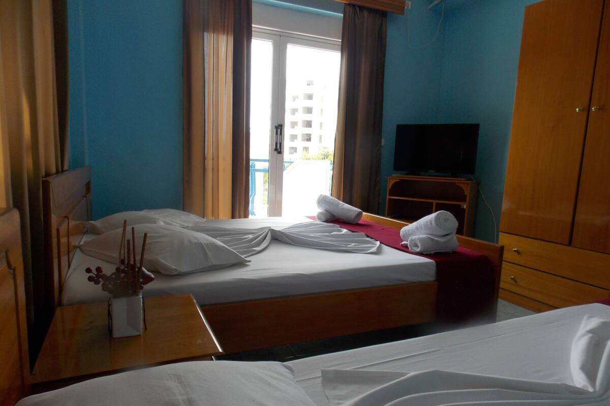 A hotel room with a bed, a TV, a wooden wardrobe, and a window with curtains.