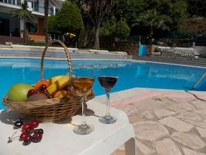 A poolside table with a fruit basket, two wine glasses, and a stone-tiled area. - Hotel Dea (Sarandë)