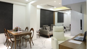 A modern living room with a dining area, a sofa, a chair, and a laptop on a desk. - Tribecca Residency (Ahmedabad)