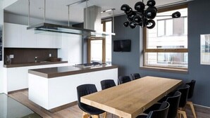 A modern kitchen with a central island, black chairs, and a wooden dining table. - Tribecca Residency (Ahmedabad)
