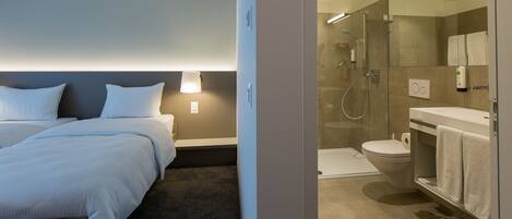 A hotel room with a bed, bedside table, and a bathroom with a shower, toilet, and sink.