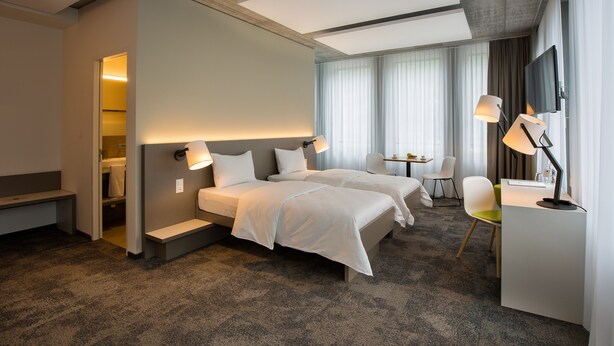 A hotel room with two beds, a desk, a chair, and a TV. - b smart motel Landquart (Landquart)