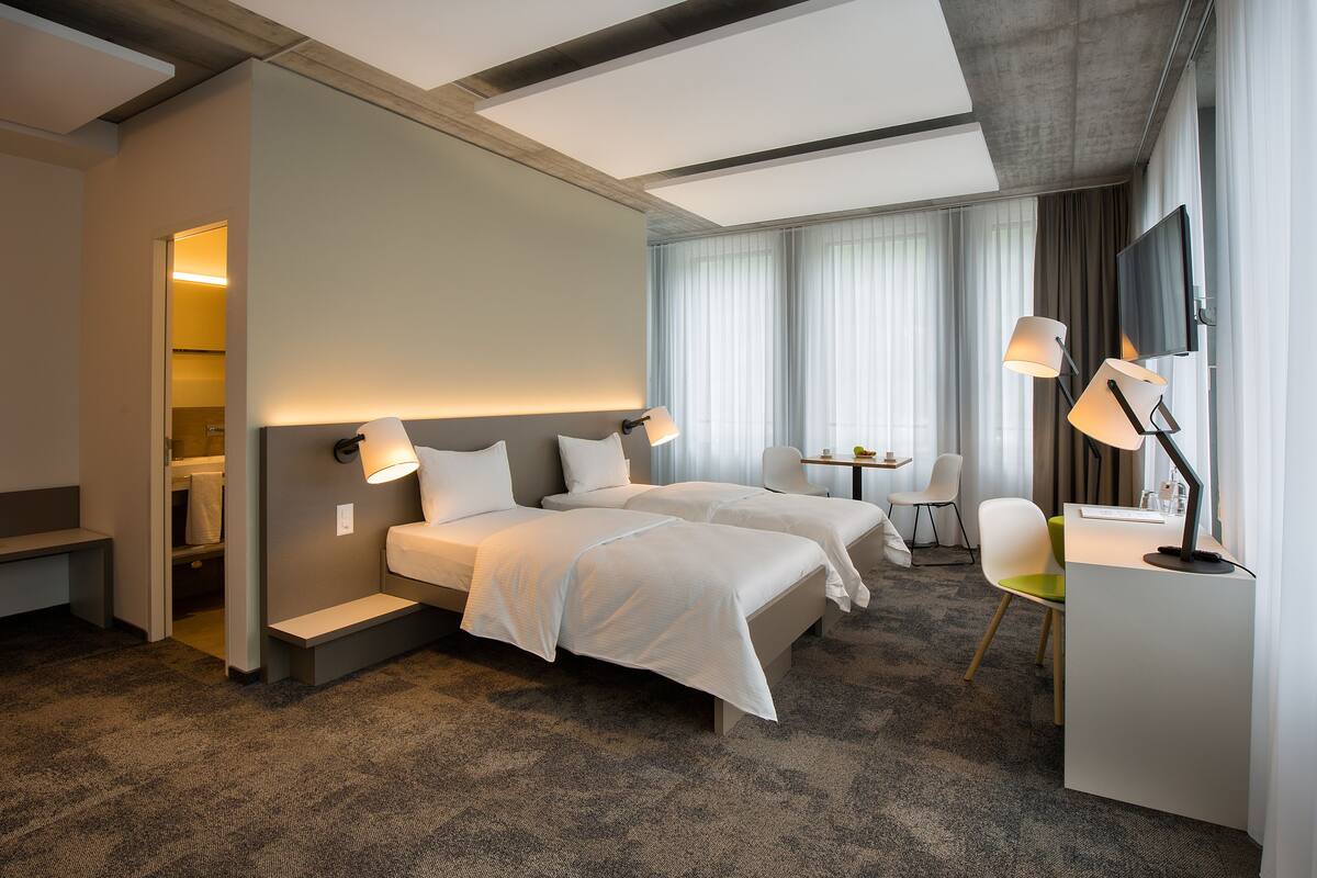 A hotel room with two beds, a desk, a chair, and a TV.