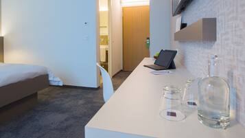 A hotel room with a bed, a desk with a laptop, a bottle, and glasses.