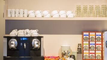 A coffee station with a Nespresso machine, stacks of white cups, glassware, and a display of Althaus coffee packaging.