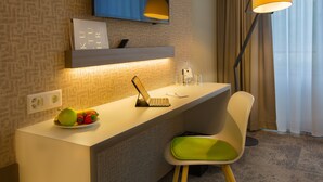 A hotel room with a desk, a chair, a laptop, a plate of fruit, a remote control, a lamp, and a TV mounted on the wall. - b smart motel Landquart (Landquart)